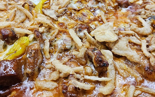The Lawn Chair pizza topped with grilled pork steak, barbecue sauce, four-cheese blend, banana peppers, and crispy fried onions